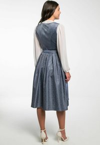 Blauw fluwelen jurk van een gemusterd stof met een aansluitend lijfje, geplooide rok en lange doorzichtige mouwen. Verfraaid met een knoop aan de achterkant en een tailleband.