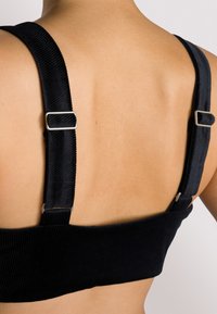 Top corto in corduroy nero con spalline regolabili. Presenta un tessuto textured con un design aderente e dettagli in hardware argentato sulle spalline.