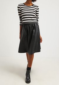 Black and white striped sweater with long sleeves, paired with a black leather skirt. Model wears black ankle boots.