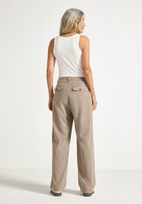 Beige rutiga byxor med hög midja och vida ben. Har två bakfickor med knappstängningar. Bärs med en vit tanktop.