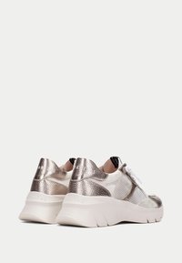 Sneakers atletici metallici argento e beige con rete testurizzata e accenti lisci. Presentano lacci bianchi e un tallone imbottito per supporto.