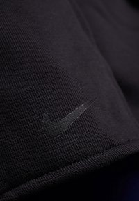 Gros plan sur un tissu noir texturé avec un logo Nike swoosh gris foncé subtil sur une couture visible.