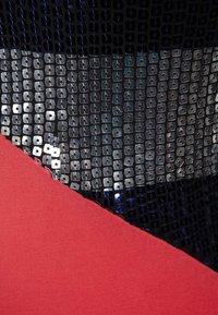 Tissu noir avec des paillettes sur le dessus, présentant un tissu rouge lisse en dessous. Les paillettes sont carrées avec de petits trous, créant un motif texturé.