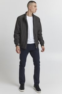 Black bomber jacket with elastic cuffs and collar, worn over a white t-shirt, paired with dark blue pants and black sneakers.