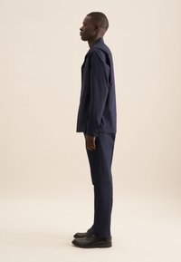 Completo di camicia e pantaloni navy, con camicia colletto e tasca sul petto. Tessuto morbido e vestibilità su misura. Scarpe nere completano l'outfit.