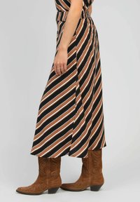 Jupe maxi rayée noire, brune et blanche avec une taille cintrée, assortie à des bottes de cowboy brunes avec un design décoratif.