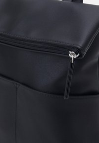 Sac à dos noir en matériau synthétique lisse, avec une fermeture zippée et une poche frontale avec une fermeture éclair verticale.