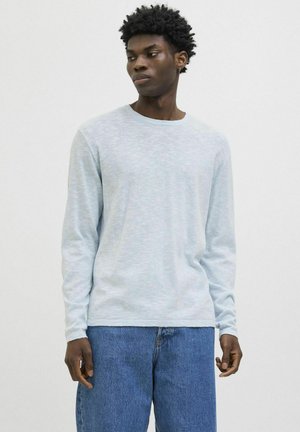Light blue long-sleeve t-shirt in soft, textured fabric with a round neckline, paired with loose blue denim jeans.