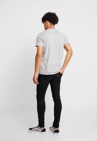 Γκρι βαμβακερή μπλούζα, κοντό μανίκι, στρογγυλή λαιμόκοψη, συνδυασμένη με μαύρα skinny jeans και μαύρα-άσπρα καρό αθλητικά παπούτσια. Πίσω όψη.