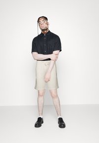 Chemise noire à manches courtes avec boutons, short beige à rayures avec cordon de serrage, et chaussures noires à lacets. Design simple avec une coupe décontractée.