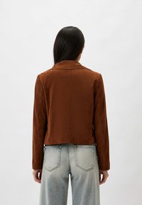 Bruine, cropped jas met een zachte textuur, geknipt revers en lange mouwen, gecombineerd met lichtgekleurde, hooggehakte spijkerbroeken.