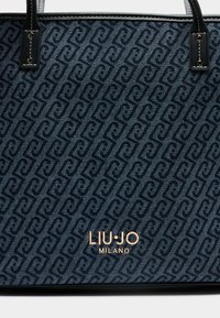 Borsa tote con motivo blu in tessuto strutturato che presenta un design ricorrente, dettagli neri e un logo metallico dorato sul davanti.