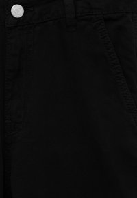 Gros plan sur un jean en denim noir montrant la poche avant, la boucle de ceinture, la couture et un bouton métallique avec du texte.