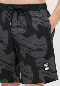 Shorts de bain noirs avec un motif abstrait tonal, taille élastique avec cordon de serrage, et un petit logo blanc sur le devant.