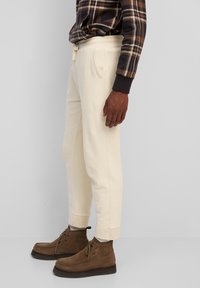Cremefarbene Sweatpants mit schmal zulaufendem Design, ausgestattet mit Seitentaschen und gerippten Bündchen, kombiniert mit braunen Wildleder-Stiefeletten.
