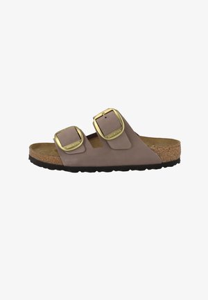 Bruine Birkenstock-sandaal met twee verstelbare gouden gespen, kurken voetbed en zwarte, getextureerde zool.