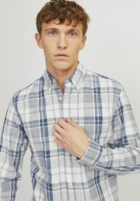 Camisa de botón con un patrón de cuadros azul y blanco, con manga larga y cuello. Fabricada con una tela ligera.