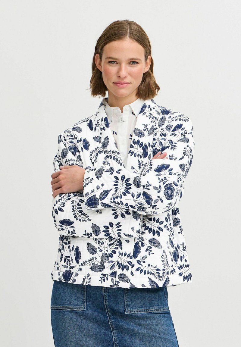 Balts ar ziedu rakstu žakets ar tumši zilu dizainu; satur klasisku apkakli un brīvu piegriezumu, apvienots ar džinsa svārkiem.