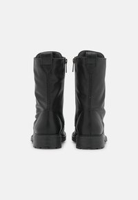Bottines en cuir noir avec une finition lisse, fermeture éclair à l'arrière et semelles texturées. Présente des coutures et un talon renforcé.