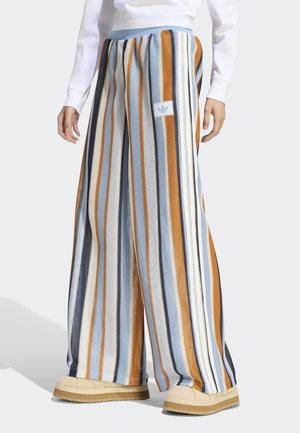 Osoba koja nosi široke pletene hlače s okomitim prugama u plavoj, bijeloj, narančastoj i crnoj, uparene s bež platformskim cipelama.