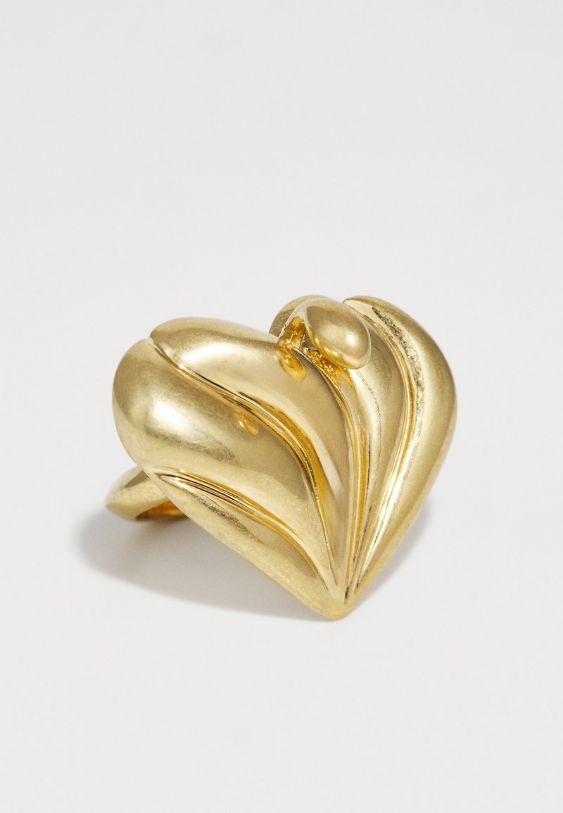 Anello a forma di cuore in oro con una finitura liscia e lucida, caratterizzato da linee curve e rialzate e un accento arrotondato sulla parte superiore.