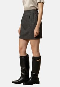 Gonna mini in tessuto grigio con pieghe e vita alta, abbinata a stivali neri in pelle alti fino al ginocchio con un accento dorato.