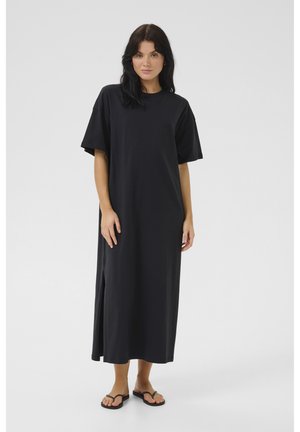 Black, knee-length T-shirt dress made of soft fabric with short sleeves, side slits, and a relaxed fit. Worn with black flip-flops.