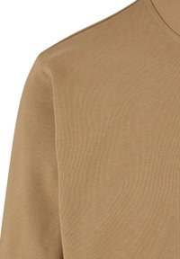 Gros plan d'une chemise marron à manches longues montrant l'épaule et la partie supérieure de la poitrine avec une texture de tissu tricoté visible.
