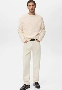 Kremowy sweter w sploty z okrągłym dekoltem, zestawiony z ecru spodniami o prostych nogawkach i czarnymi skórzanymi butami, minimalistyczny design.