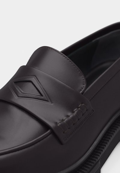 Μαύρο δερμάτινο παπούτσι τύπου loafer με ανάγλυφη λεπτομέρεια σε σχήμα ρόμβου στο λουράκι και ορατή υφασμένη λαστιχένια σόλα.