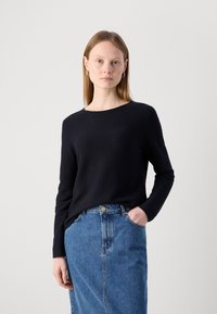 Črna dolga majica s dolgimi rokavi iz pletenega materiala, z okroglo izrezom. V kombinaciji z visokim modrim denim krilom.