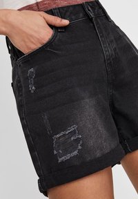 Pantalones cortos de mezclilla negra con un acabado desgastado, que presentan áreas desgastadas y dobladillos enrollados. Diseño de cinco bolsillos con detalles de costura visibles.