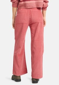 Rode corduroy wijde broek met achterzakken en zichtbare ribbeltextuur. Gekocht met bruine schoenen, gezien vanaf de achterkant.