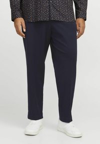 Pantalons bleus à rayures, avec une coupe droite, un tissu texturé et un léger brillant, associés à des baskets blanches.