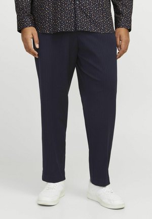 Pantalons bleus à rayures, avec une coupe droite, un tissu texturé et un léger brillant, associés à des baskets blanches.