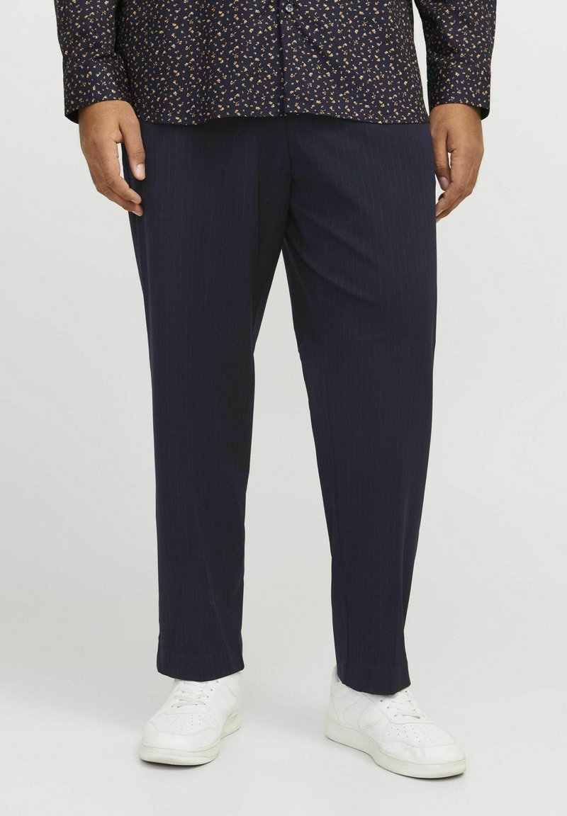 Pantalons bleus à rayures, avec une coupe droite, un tissu texturé et un léger brillant, associés à des baskets blanches.