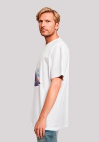 Weiße Baumwoll-T-Shirt mit lockerer Passform, featuring ein farbenfrohes Bergmotiv auf der Vorderseite. Kurze Ärmel und Rundhalsausschnitt.