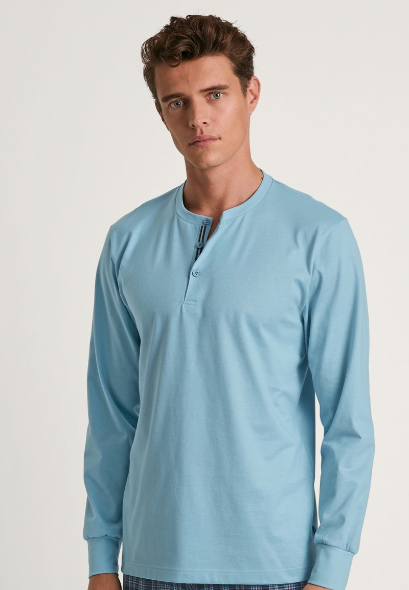 Lichtblauwe langslievende top met een henley halslijn, voorzien van twee knopen en een rechte zoom. Glad materiaal en aansluitende manchetten.