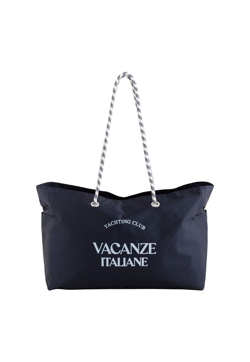Laukku merensiniseen väriin, jossa valkoisella tekstillä "YACHTING CLUB" ja "VACANZE ITALIANE", köysikahva ja pehmeä, kestävä kangas.