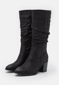 Botas altas hasta la rodilla de color negro, fabricadas en suave ante, con un diseño relajado, punta afilada, costuras decorativas y un tacón grueso.