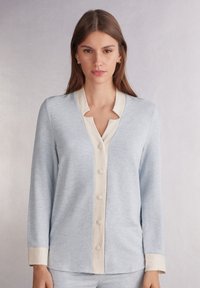 Hellblaue Langarmbluse aus weichem Stoff mit krèmfarbigem Kragen und Knopfleiste; sie hat einen Schlüsselloch-Ausschnitt und Manschetten.