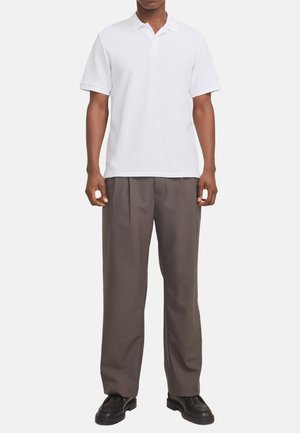 Weißes Poloshirt mit kurzen Ärmeln, strukturiertem Stoff, zwei-Knopf-Leiste; kombiniert mit lockeren grauen Hosen und schwarzen Schuhen.