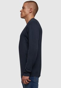 Mørkeblå langermet genser i en tettsittende design, laget av myk stoff med ribbestrikket mansjetter og kant, vist på en modell fra siden.