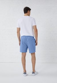 Pantaloni da bagno azzurri chiari con vita elastica e tasca posteriore. Abbinati a una t-shirt bianca e sneakers bianche. Tessuto morbido, design casual.
