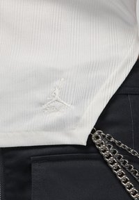 Maglietta bianca a coste con logo Jumpman ricamato e firma. Abbinata a un tessuto scuro e un accento di catena argentata.