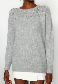 Hellgrauer Strickpullover mit Rundhalsausschnitt, gerippter Textur und Verzierungen aus klaren Perlen entlang der Schultern.