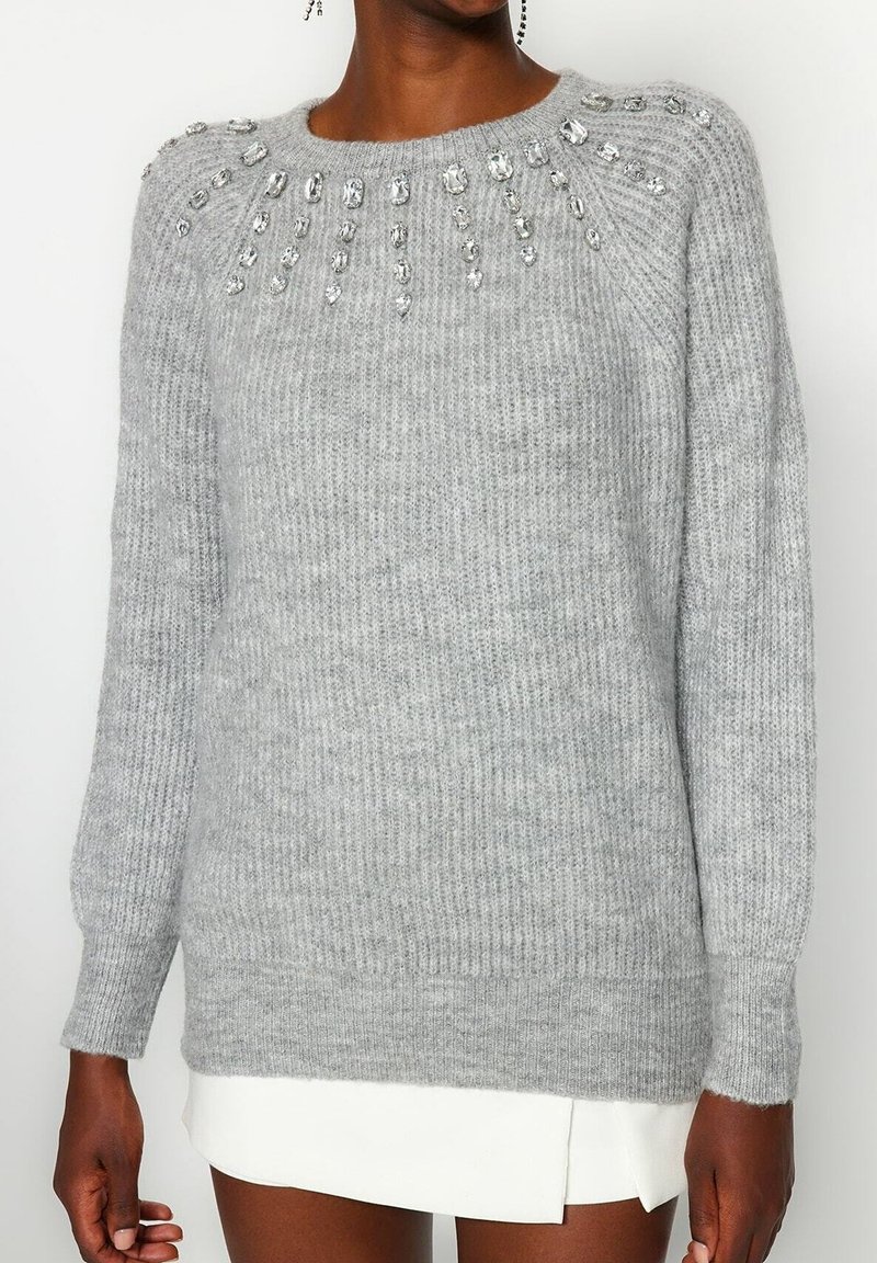 Hellgrauer Strickpullover mit Rundhalsausschnitt, gerippter Textur und Verzierungen aus klaren Perlen entlang der Schultern.