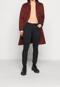 Lång vinröd kappa med skräddarsydd design, matchad med en strukturerad persikofärgad kort trikåtröja, svarta cargobyxor och svarta snörstövlar.