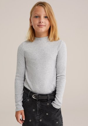 Top de manga larga gris de canalé con cuello alto, combinado con una falda negra con ojales plateados y un cinturón negro.