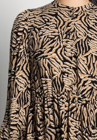 Brunt och svart mönstrad tyg med tigerrandigt mönster, med veck och en rundad halsringning med knappar i mitten.